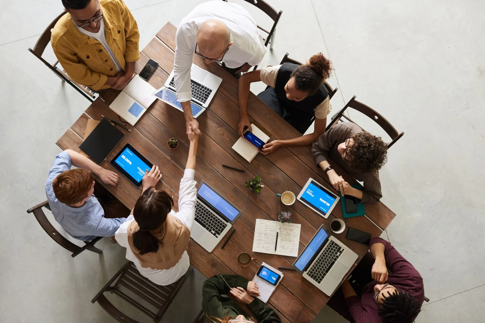 A diverse group gathered around a table with laptops, notebooks, and shared work